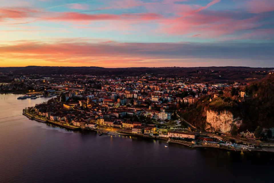 Atemberaubende Luftaufnahme des Lago Maggiore bei Sonnenuntergang in Arona, Italien, mit lebendigen Farben und historischer Architektur.